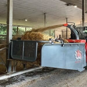 a Kubota skid steer is blowing straw in a barn with an attached straw bale blower
