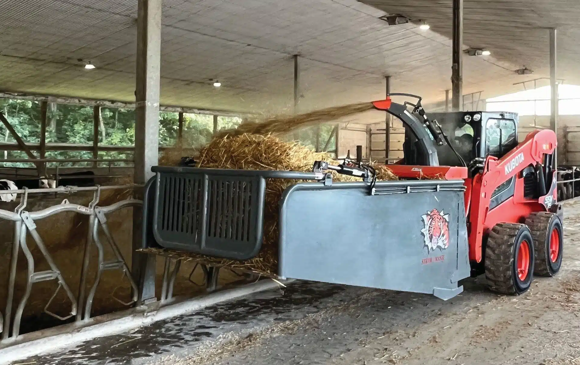 a Kubota skid steer is blowing straw in a barn with an attached straw bale blower