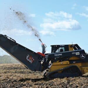 a John Deere skid steer with a straw bale blower is blowing straw in a large field for landscaping and farming purposes